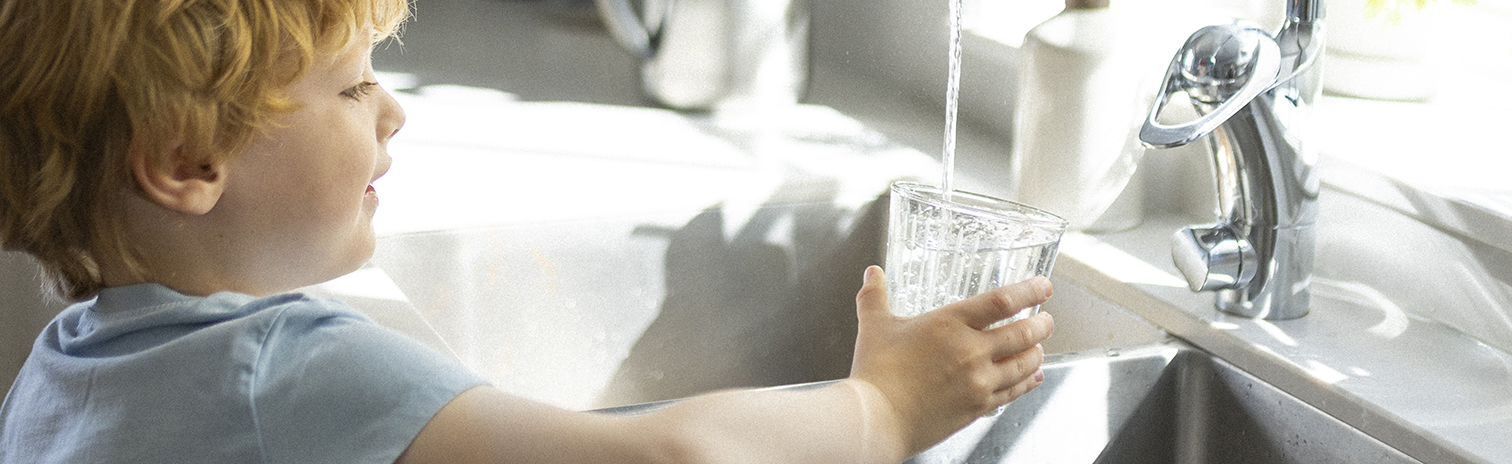 Pojke fyller ett glas med vatten under en rinnande kran